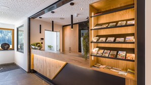 Ein Empfangsbereich mit einem Holzbüro, einem Bücherregal mit Reiseführern und einem großen Fenster mit Blick auf Bäume.
