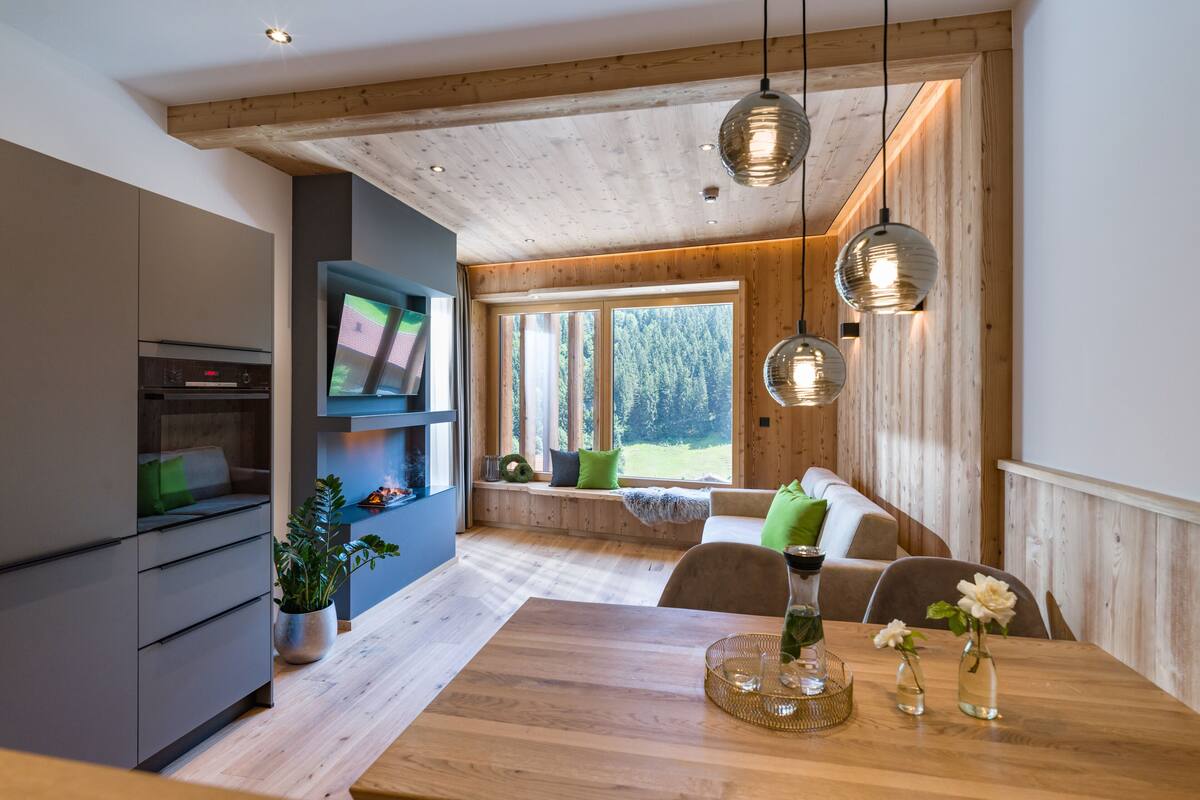 A modern kitchen with a built-in oven, a dining area with a wooden table, and a cozy seating area with a view of the outdoors.