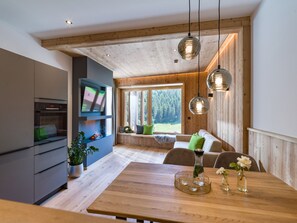 A modern kitchen with a built-in oven, a dining area with a wooden table, and a cozy seating area with a view of the outdoors.