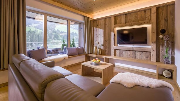 Ein gemütliches Wohnzimmer mit einer großen Couch, einem Couchtisch und einem an einer Holzwand befestigten Fernseher.