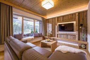 A cozy living room with a large sofa, a coffee table, and a TV mounted on a wooden wall. - Bergjuwel (Wildschönau)
