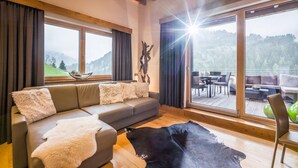 Ein modernes Wohnzimmer mit großem Fenster, einer Couch, einem Lederteppich und einem Essbereich, der durch das Fenster sichtbar ist.