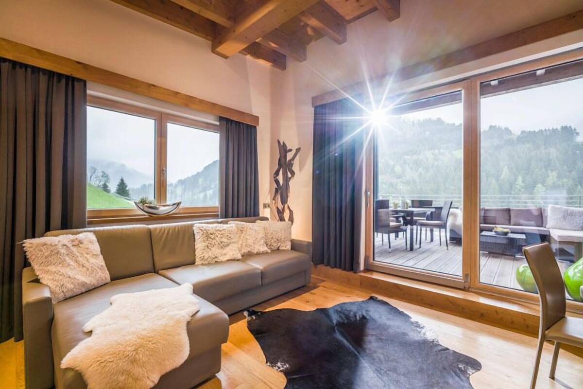 A modern living room with a large window, a sofa, a leather rug, and a dining area visible through the window.