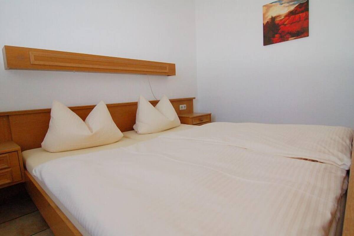 Een slaapkamer met een houten bedframe, witte beddengoed en een nachtkastje.