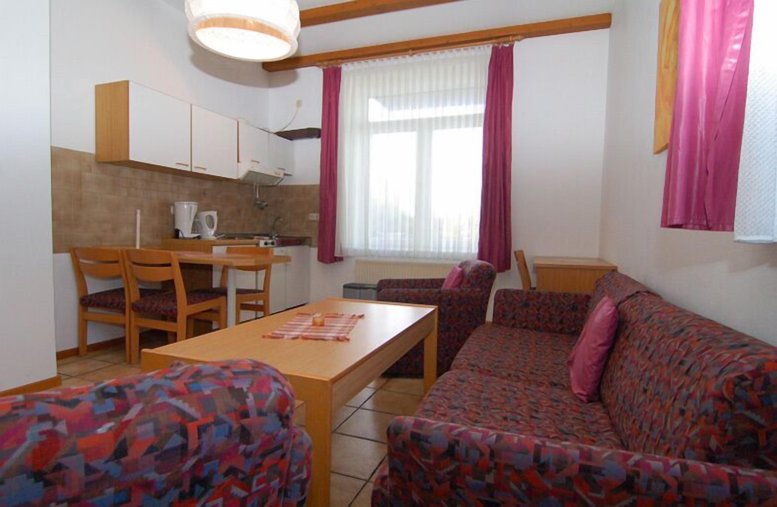 A small, furnished room with a sofa, a dining table, and a kitchenette.
