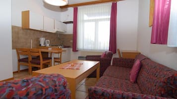 A small, furnished room with a sofa, a dining table, and a kitchenette.