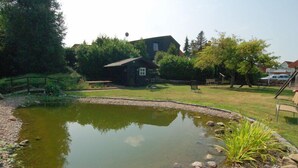 Un étang avec un pont en bois, une petite cabane et une végétation luxuriante tout autour.