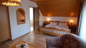 Une chambre avec un plafond en bois, un lit recouvert de draps blancs, deux lampes de chevet, un miroir et une chaise en osier.