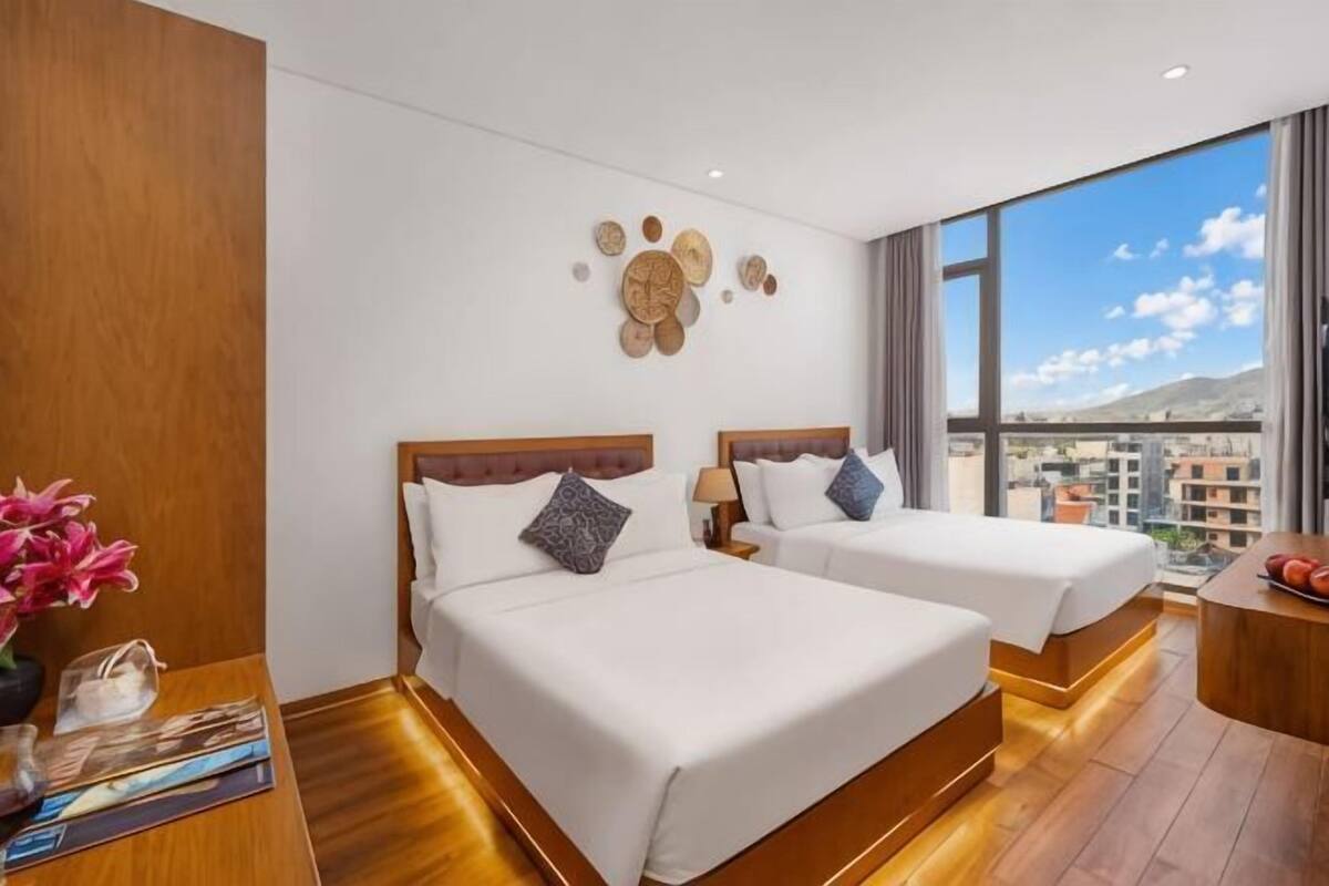 A hotel room with two beds, a wooden floor, a city view, and a decorative wall.