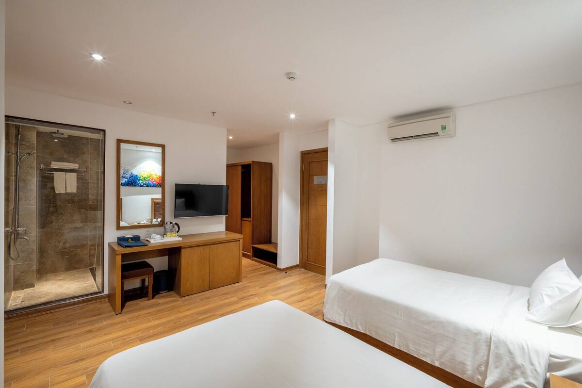 A hotel room with a shower, a desk, a TV, and two beds.