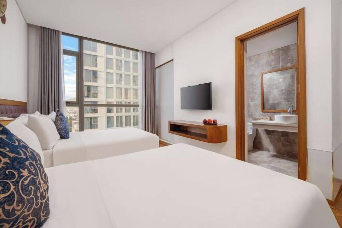 A hotel room with two beds, a TV, a small TV stand, a bathroom with a mirror, and a large window.