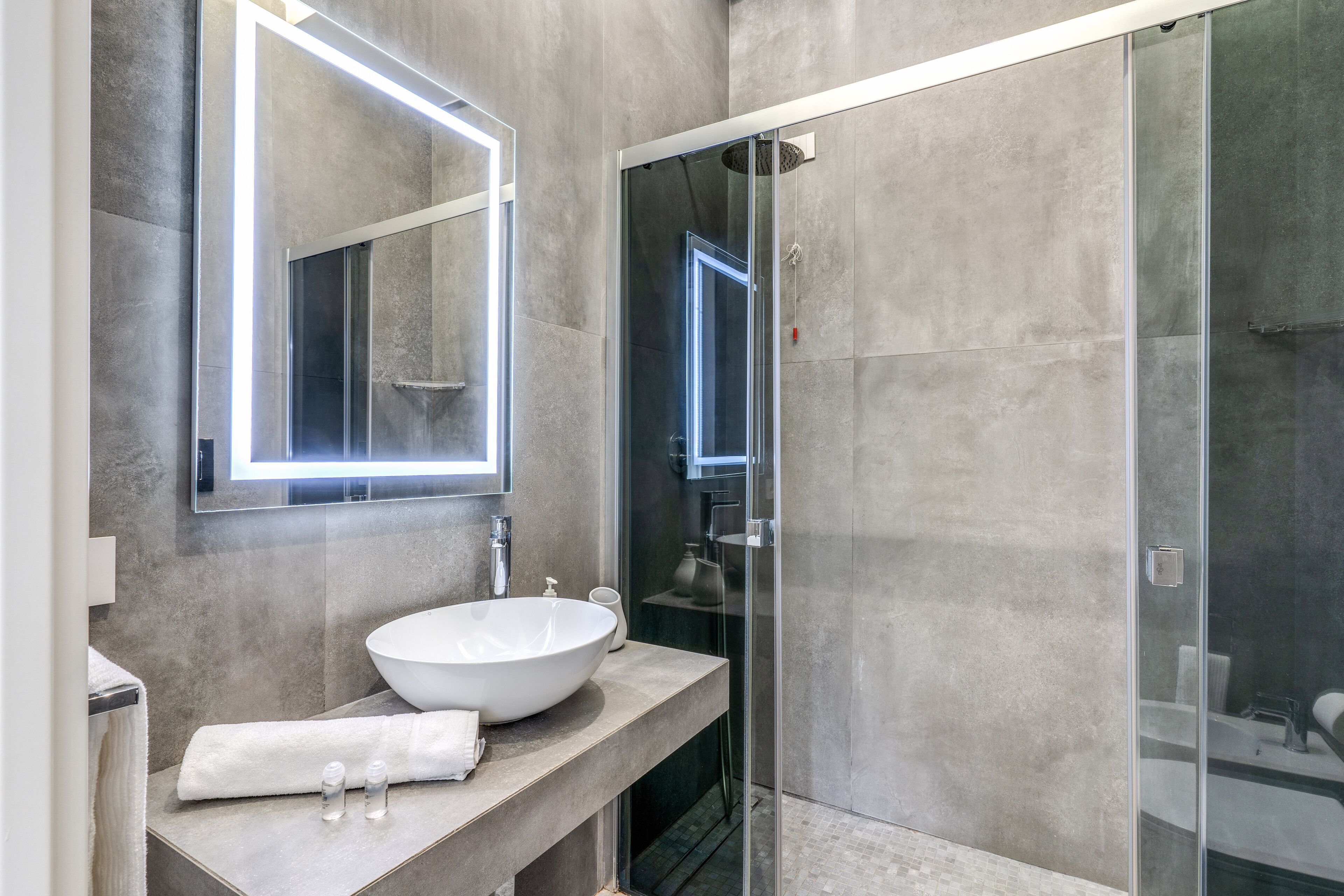 Un baño moderno con un lavamanos grande de color blanco, un box de ducha de vidrio e iluminación integrada en un espejo.