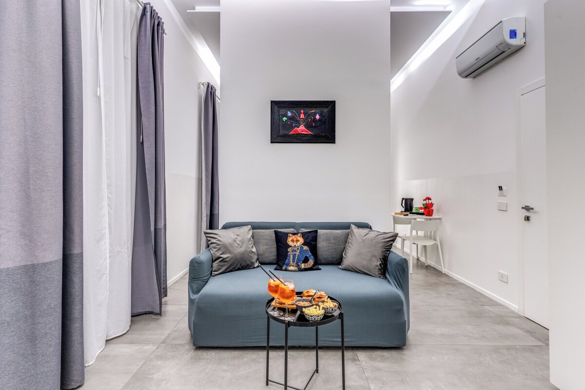 A modern living room with a sofa, a small table with drinks, and a wall-mounted air conditioner.