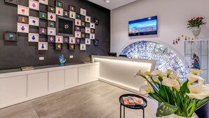 Un espace d’accueil moderne avec un mur noir où sont exposées des sculptures colorées, un grand écran de télévision et une fenêtre décorative en verre.