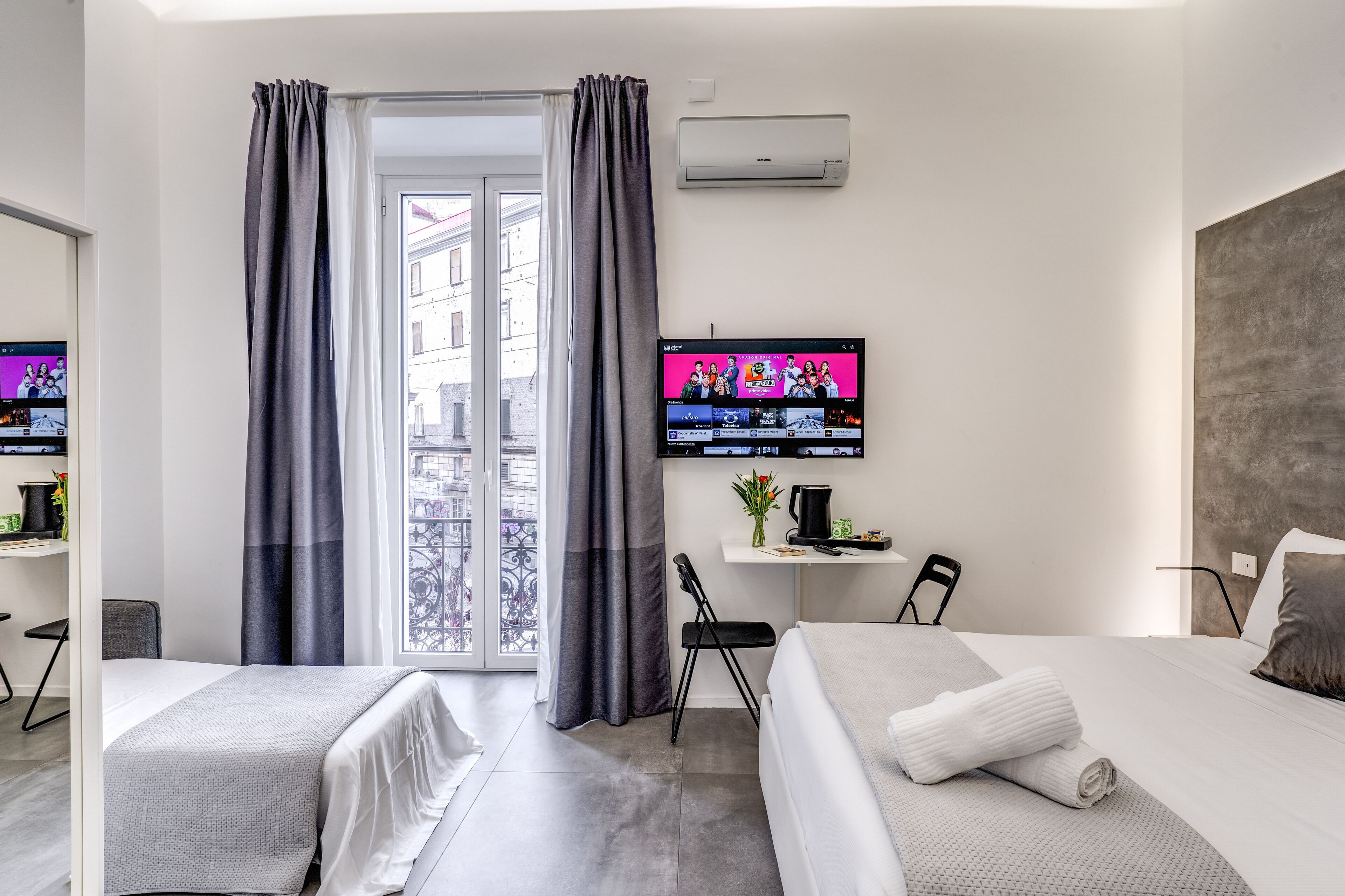 Una habitación de hotel moderna con dos camas, un escritorio, un televisor y un balcón con cortinas.