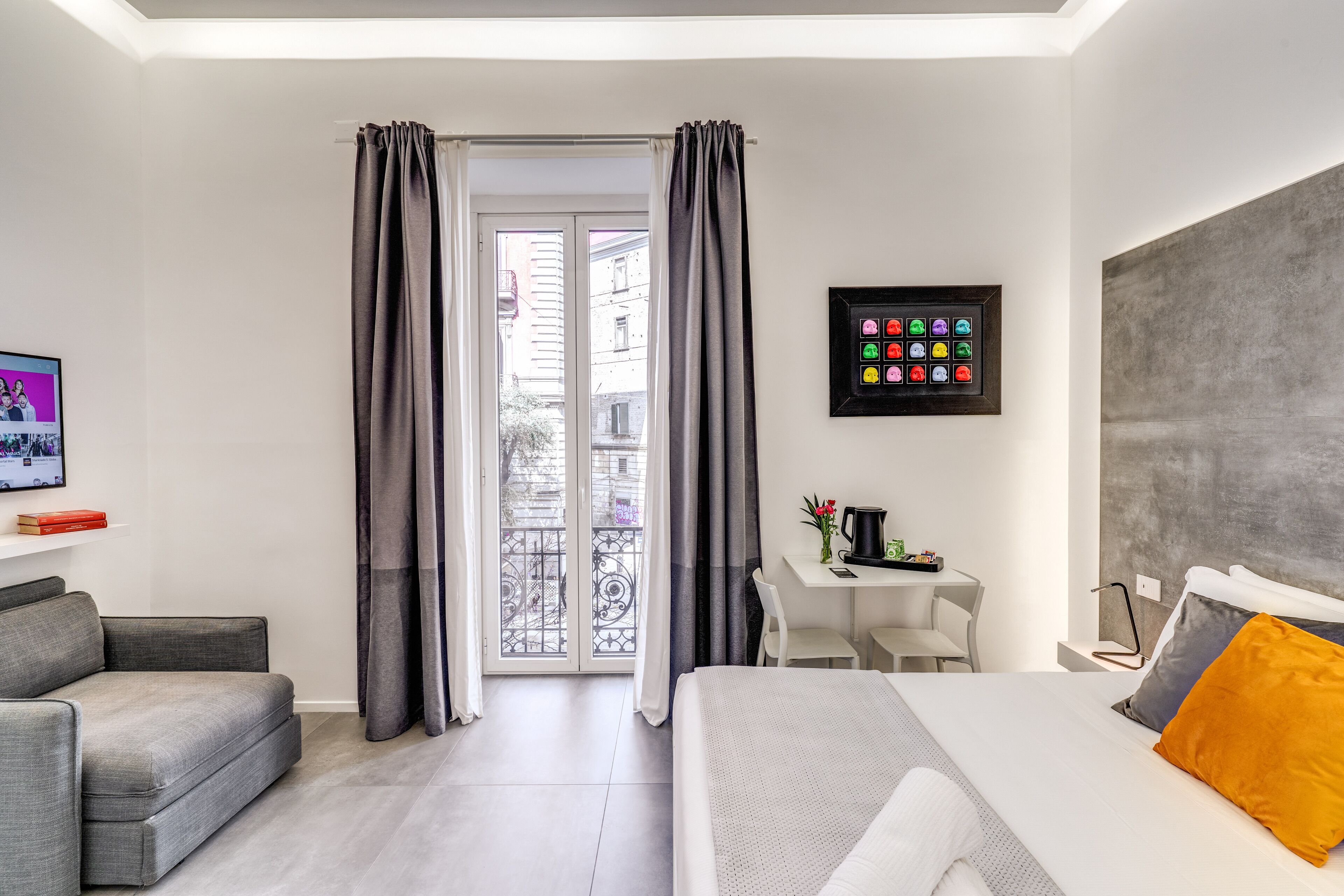 A modern hotel room with a bed, a sofa, a desk, and a balcony with curtains.