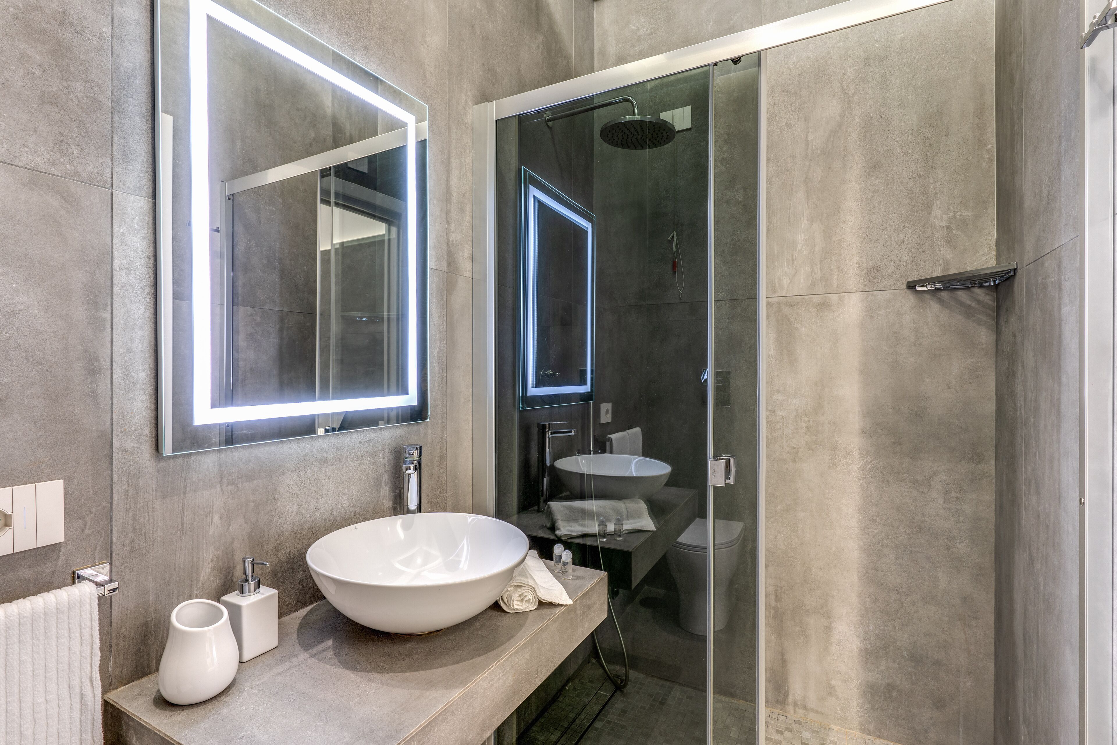 Een moderne badkamer met een grote spiegel, een wastafel op voet en een douche met glazen wanden.