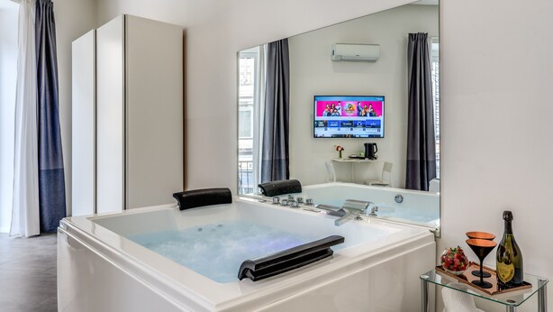 Une salle de bain moderne dotée d’une grande baignoire, d’un meuble-lavabo avec un plateau en verre et d’un téléviseur à écran plat fixé au mur.