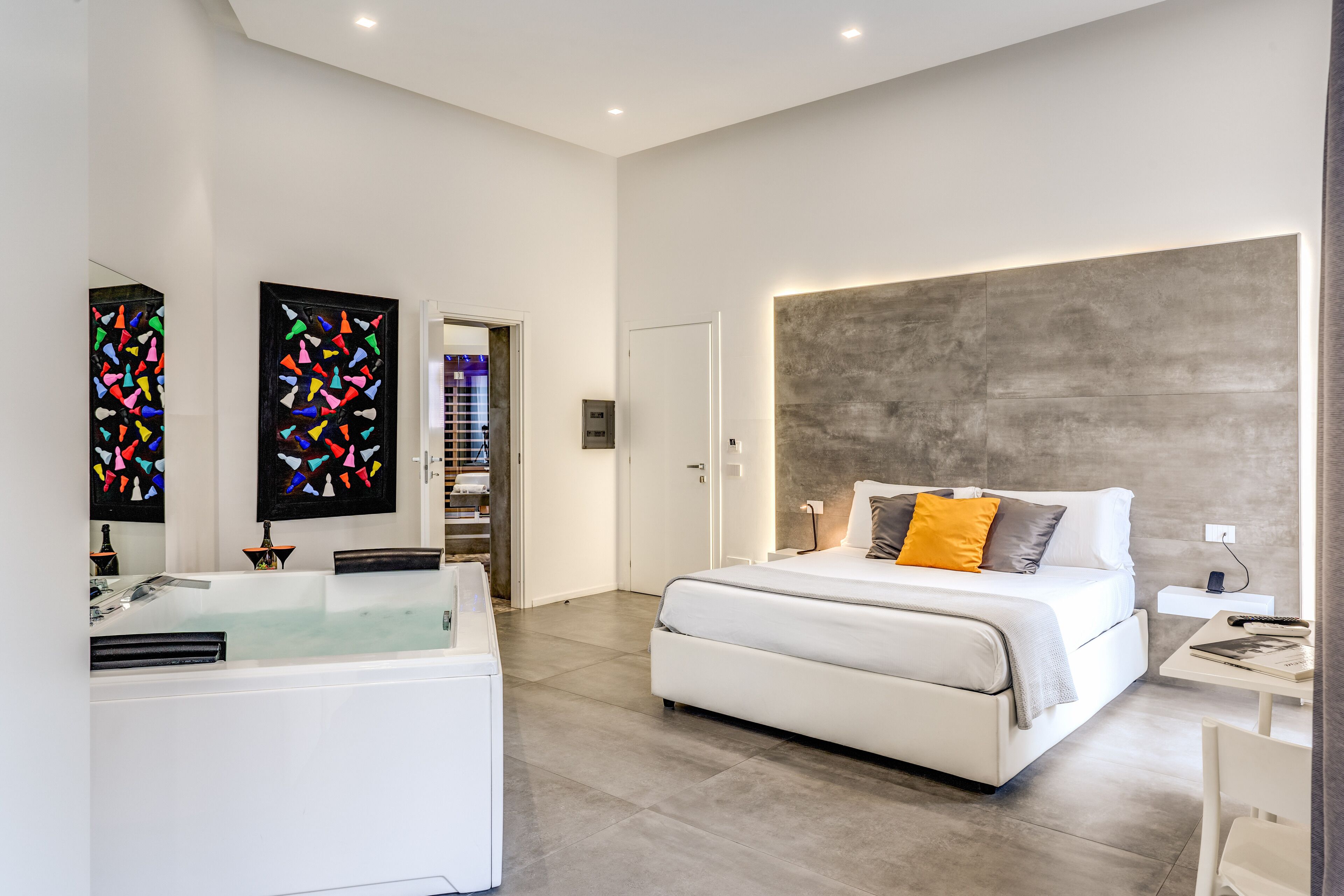 Una camera da letto moderna con un letto grande, una vasca idromassaggio integrata e un'ampia opera d'arte a parete.