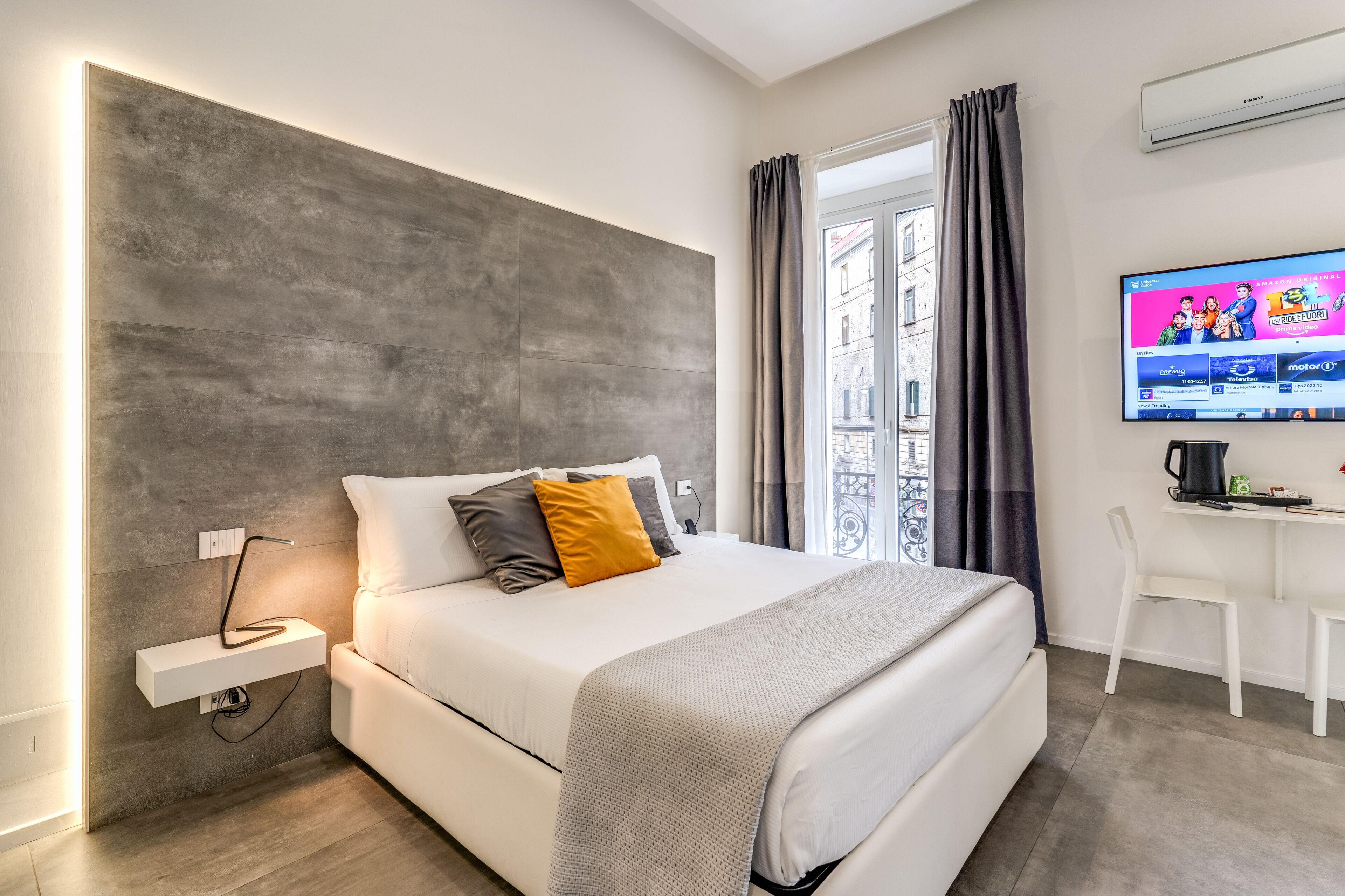A modern hotel room with a large bed, a bedside table, a flat-screen TV, and a window with curtains.