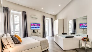 Une chambre d’hôtel moderne équipée d’un lit, d’un bureau, d’un grand miroir, d’une baignoire et d’un téléviseur.