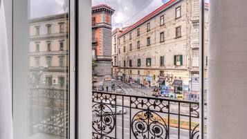 Vista da un balcone con ringhiera in ferro battuto, su una strada con edifici e un cielo sereno.