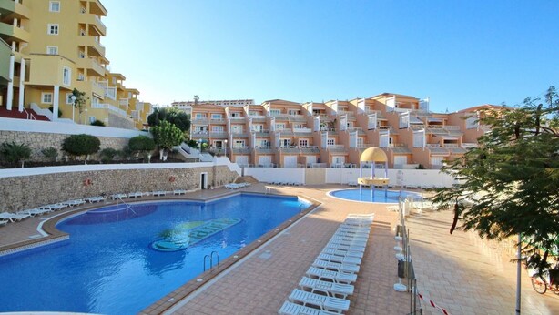 A swimming pool with lounge chairs and a building with balconies in the background. - Apartment with a pool in Costa Adeje (Adeje)