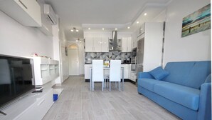 A modern kitchen with white cabinets, a dining area with a table and chairs, and a blue sofa in a living area. - Apartment with a pool in Costa Adeje (Adeje)