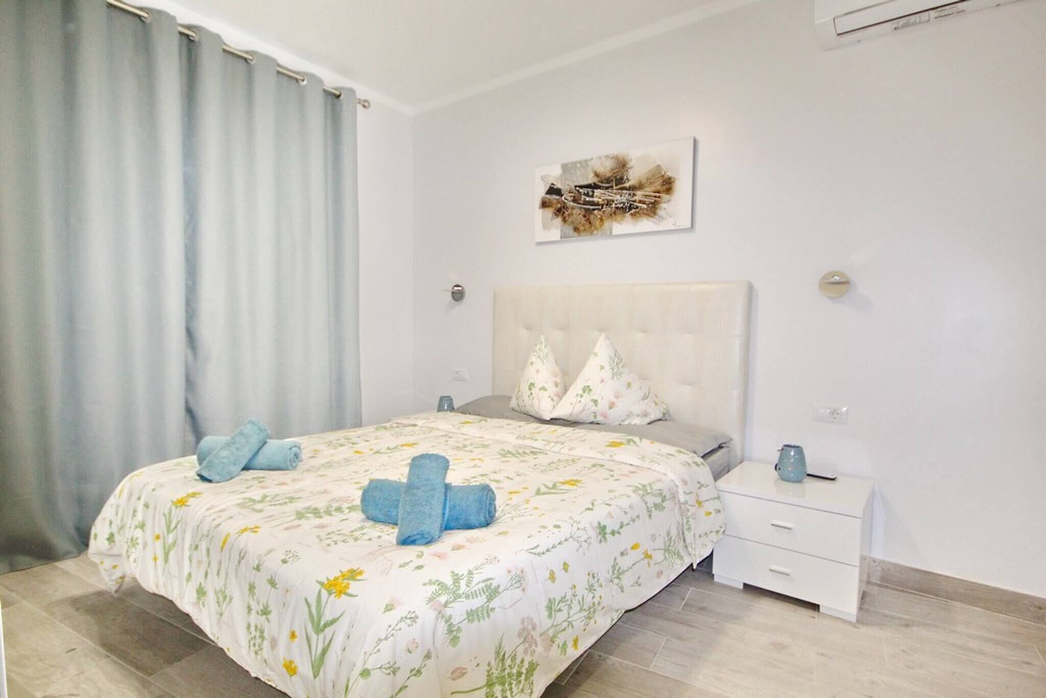 Een slaapkamer met een bed, nachtkastje, wanddecoratie en een raam met gordijnen.
