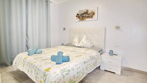 A bedroom with a bed, a nightstand, a wall-mounted artwork, and a window with curtains. - Apartment with a pool in Costa Adeje (Adeje)