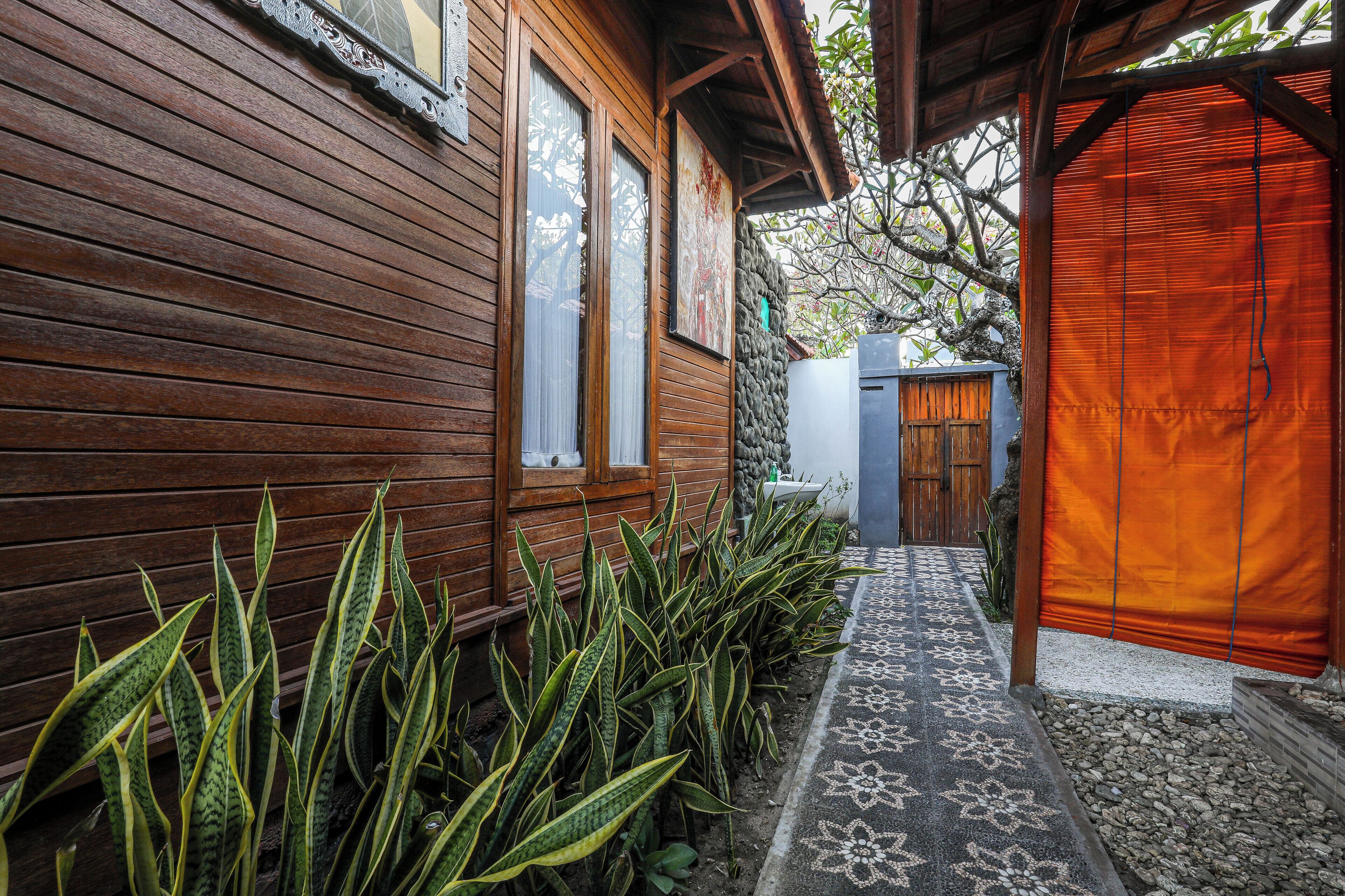A wooden house with a covered porch, a patterned walkway, and a variety of green plants.