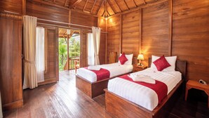 A wooden cabin with two beds, each with white linens and red accents, a wooden ceiling, and a view of greenery outside. - Swan Beach Inn (Penida Island)