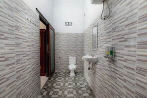 Une petite salle de bain avec des carreaux décorés, des toilettes blanches et un lavabo surmonté d’un miroir.