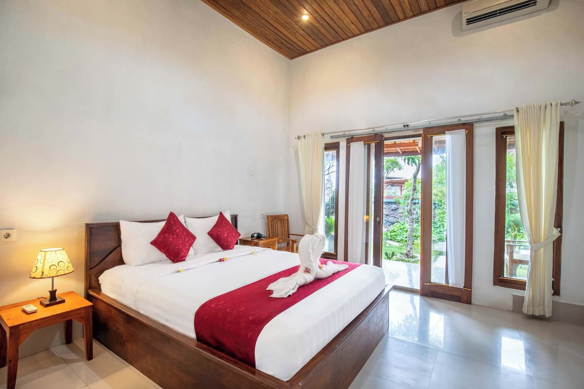 A spacious bedroom with a large bed, a nightstand, and a window with curtains.