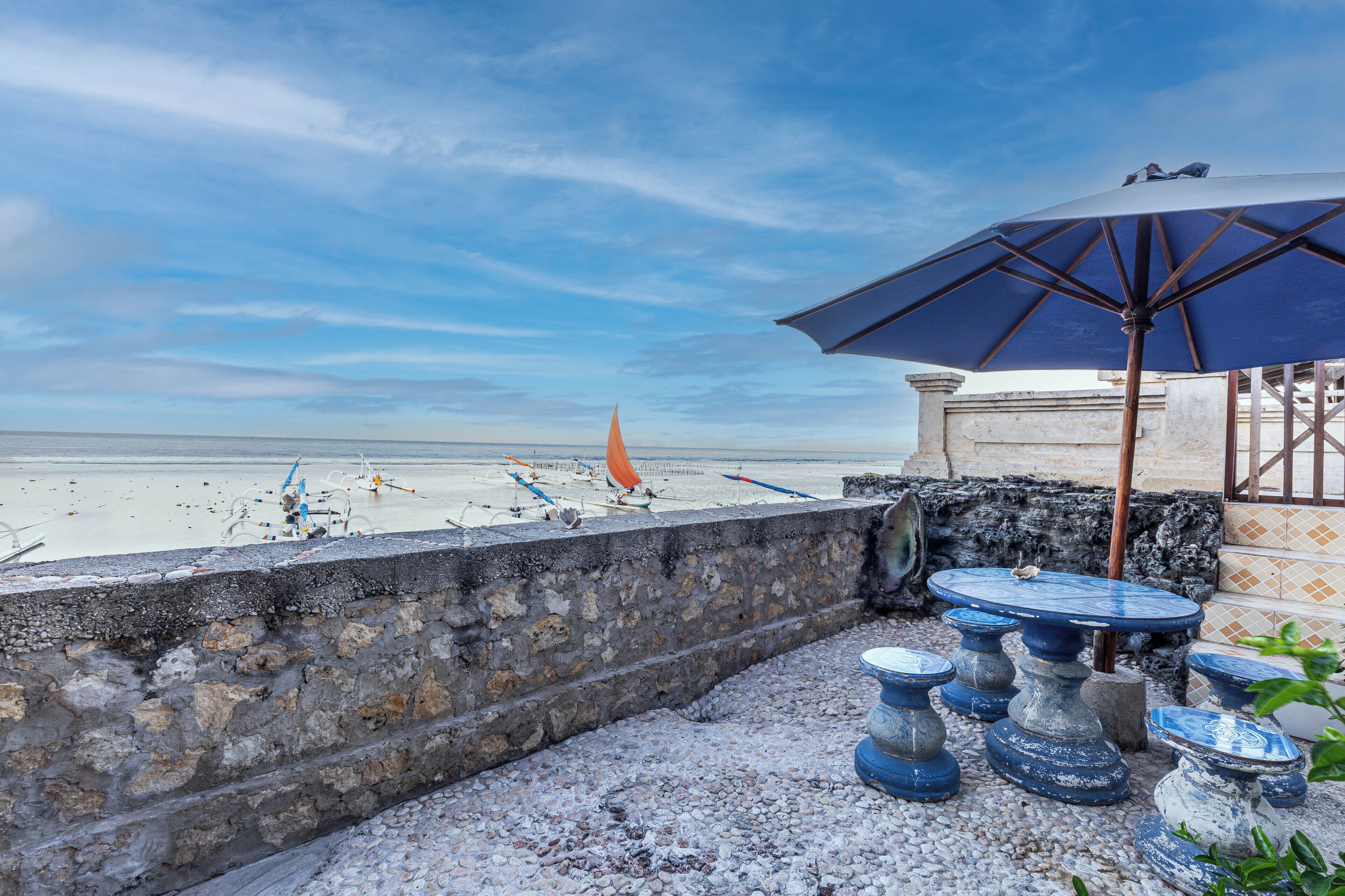 A terrace with a view of the beach, featuring a table and chairs, and a large umbrella.