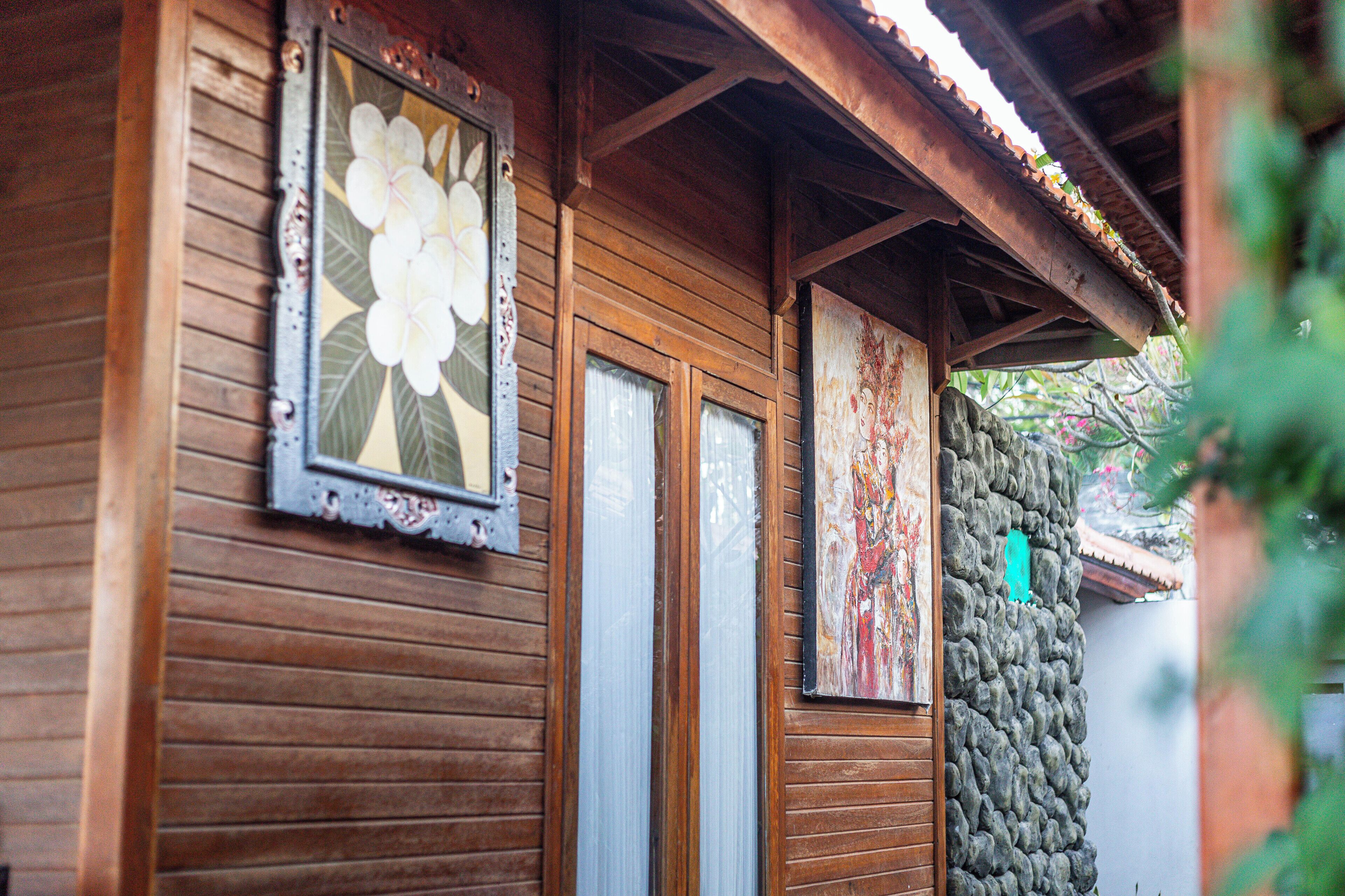 Un edificio de madera con un muro de piedra, una puerta de madera y una ventana con diseño floral.