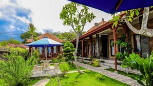 A courtyard with a stone pathway, a blue umbrella, and a variety of plants. - Swan Beach Inn (Penida Island)