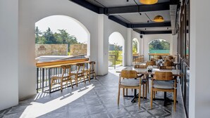 A spacious outdoor dining area with wooden tables and chairs, large windows, and a view of greenery. - The Amrta Borobudur (Borobudur)