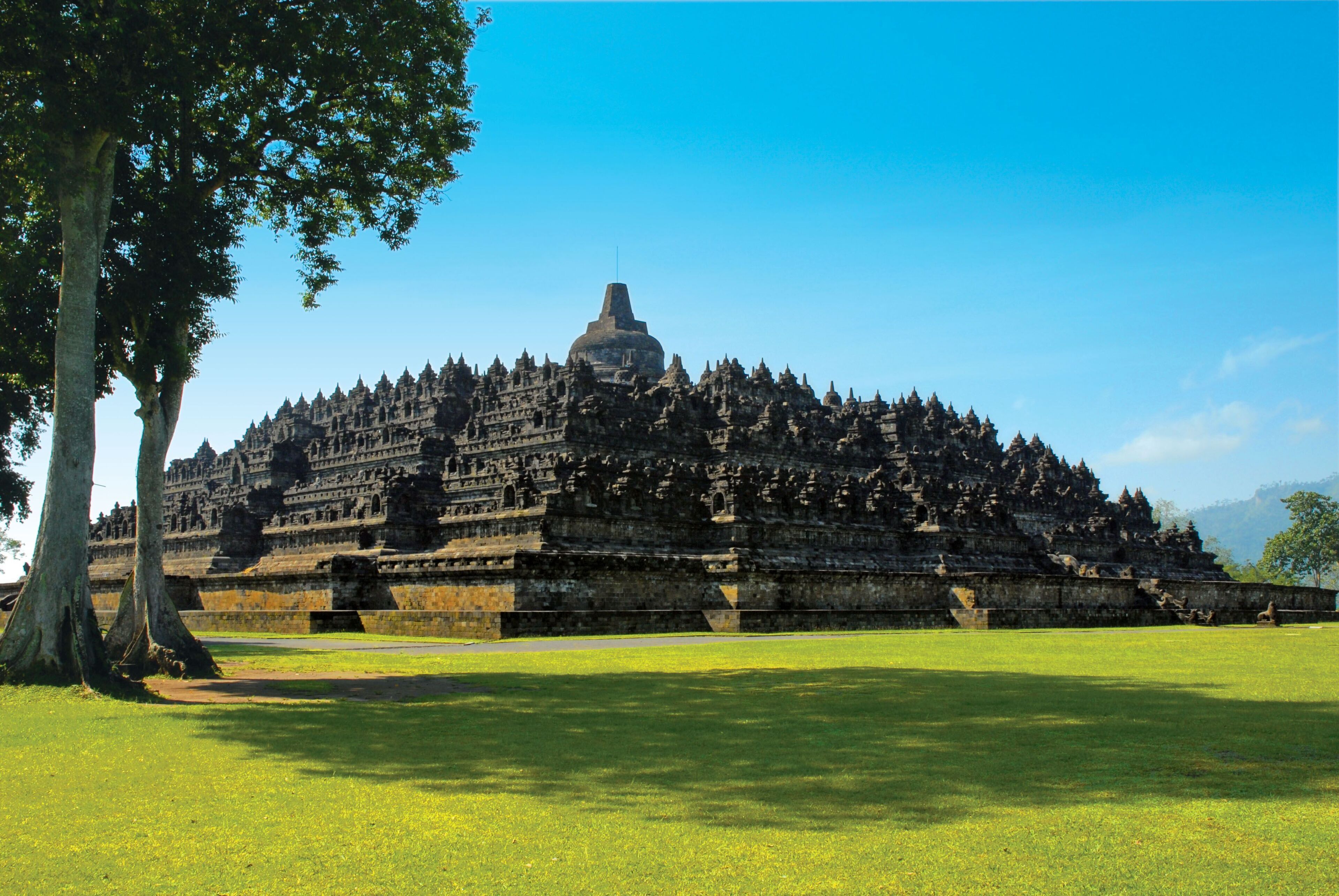 A large, multi-tiered temple complex with a central dome, surrounded by lush green grass and trees.