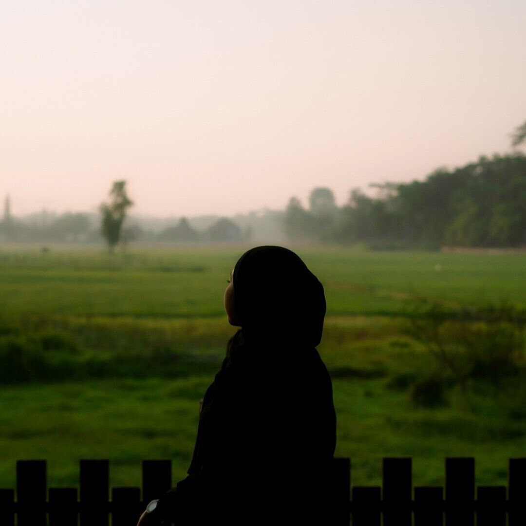 A child sitting on a wooden fence overlooking a green field.