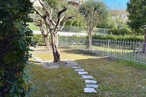 A garden with a stone pathway, trees, and a white fence.