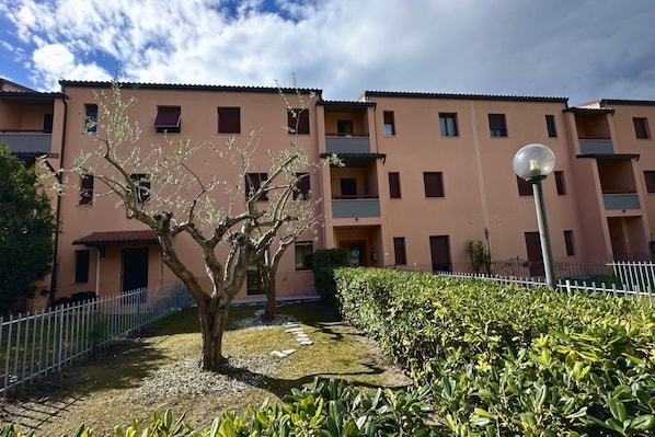 A multi-story residential building with balconies, a paved courtyard, and a street lamp.