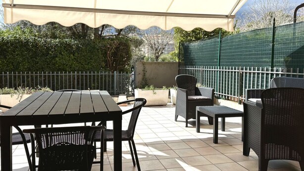 An outdoor patio with a table and chairs, a covered area, and a green fence. - S044 - Sirolo, delightful three-room apartment with garden (Sirolo)