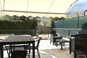 An outdoor patio with a table and chairs, a covered area, and a green fence.