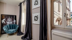 A room with a teal armchair, black curtains, a framed abstract painting, and a window with a view of a building. - Artale 07 - Adults Only (Split)