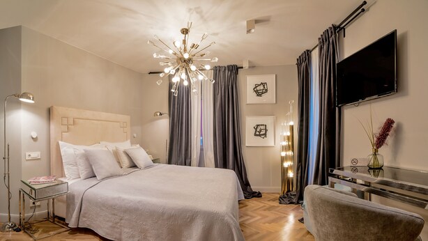 A modern bedroom with a large bed, a bedside table, a desk, a chair, a TV, and a decorative ceiling light. - Artale 07 - Adults Only (Split)