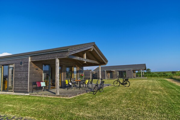 Et moderne hus med en overdækket terrasse, udendørs møbler og en cykel.