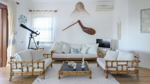 A living room with a white sofa, two bamboo chairs, a coffee table, and a telescope. - Villa Gaviel, private descent to lonely beach, scenic P. Istana, wifi (Porto Istana, Olbia)