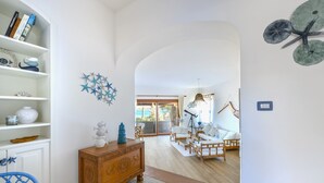 A spacious living area with a wooden floor, white walls, and a view through an archway to a balcony. - Villa Gaviel, private descent to lonely beach, scenic P. Istana, wifi (Porto Istana, Olbia)