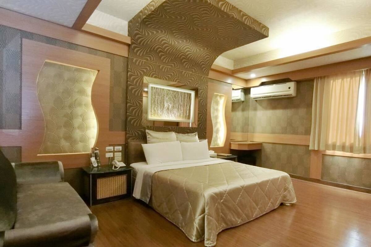 A spacious bedroom with a large bed, a bedside table, a chair, and a wall-mounted air conditioner.